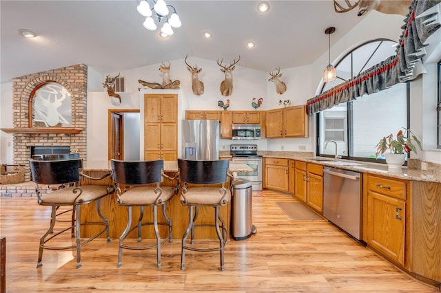 kitchen featuring light stone countertops, stainless steel appliances, sink, light hardwood / wood-style floors, and hanging light fixtures