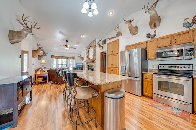 kitchen with light stone counters, a center island, stainless steel appliances, light wood-style floors, and open floor plan