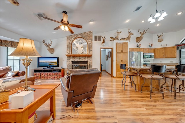 living area with ceiling fan with notable chandelier, light wood-style flooring, a fireplace, and visible vents