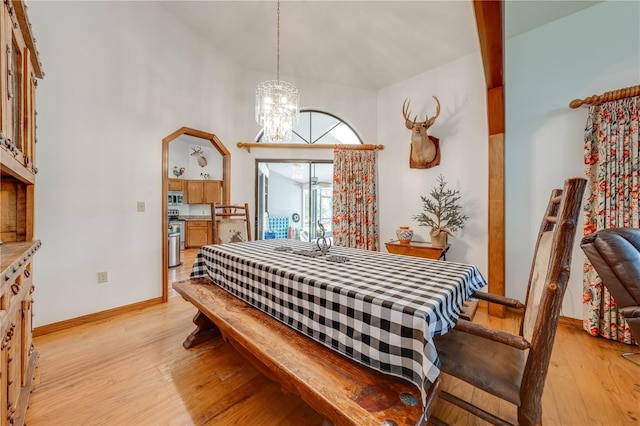 dining space featuring arched walkways, a notable chandelier, a high ceiling, light wood-style floors, and baseboards