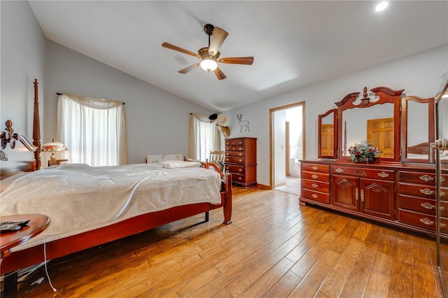 bedroom featuring light wood-type flooring, ensuite bath, vaulted ceiling, and ceiling fan