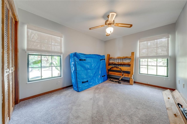 carpeted bedroom with a ceiling fan, multiple windows, and baseboards