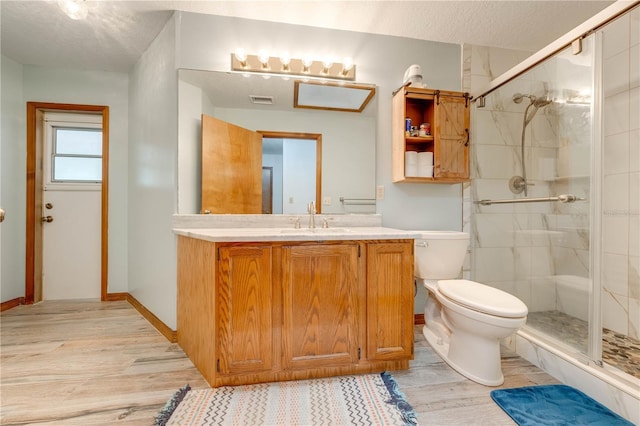 bathroom featuring vanity, a shower with door, toilet, a textured ceiling, and wood-type flooring