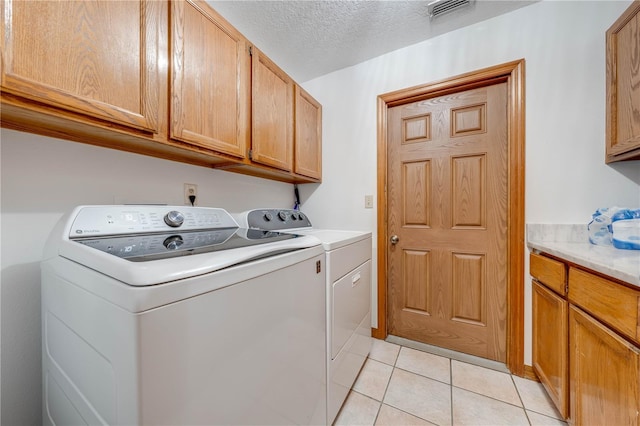 laundry room featuring washer and dryer, cabinets, light tile patterned floors, and a textured ceiling