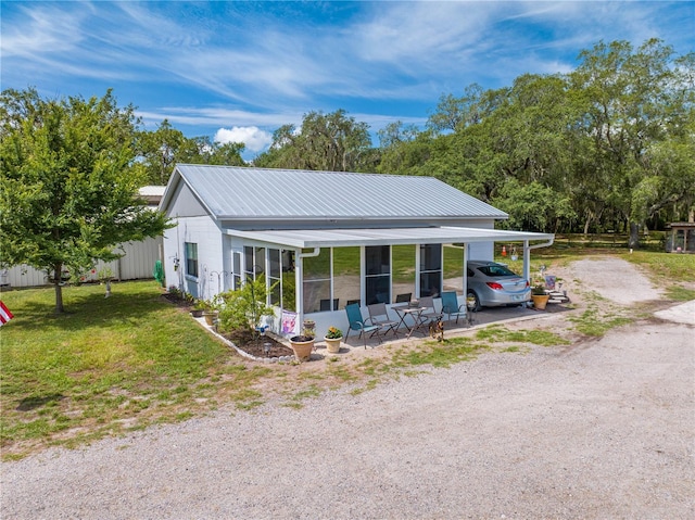 view of front facade featuring a sunroom, metal roof, driveway, and a front lawn