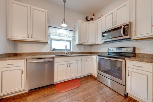 kitchen featuring white cabinetry, sink, hanging light fixtures, appliances with stainless steel finishes, and light wood-type flooring