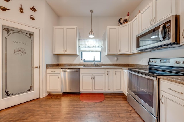 kitchen featuring hanging light fixtures, sink, light hardwood / wood-style flooring, appliances with stainless steel finishes, and white cabinetry