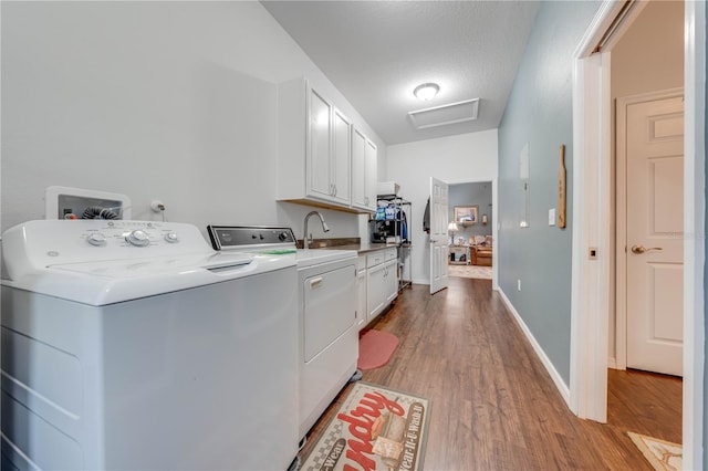 washroom with cabinet space, attic access, light wood-style flooring, and washing machine and clothes dryer