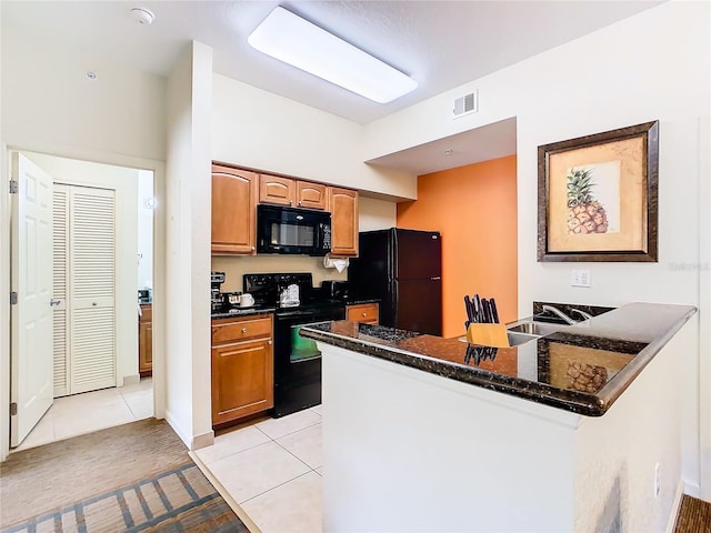 kitchen featuring dark stone counters, light tile patterned flooring, black appliances, sink, and kitchen peninsula