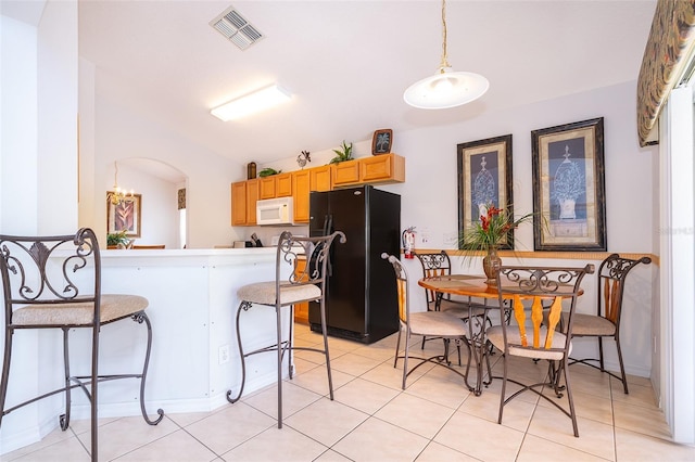 kitchen with kitchen peninsula, black fridge, light tile patterned floors, hanging light fixtures, and a breakfast bar area