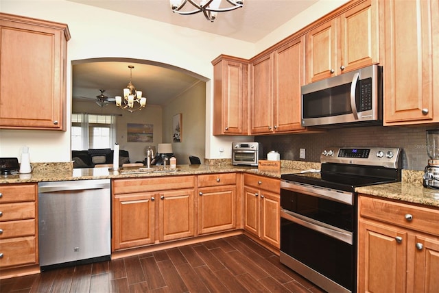 kitchen featuring appliances with stainless steel finishes, light stone counters, ceiling fan with notable chandelier, sink, and pendant lighting