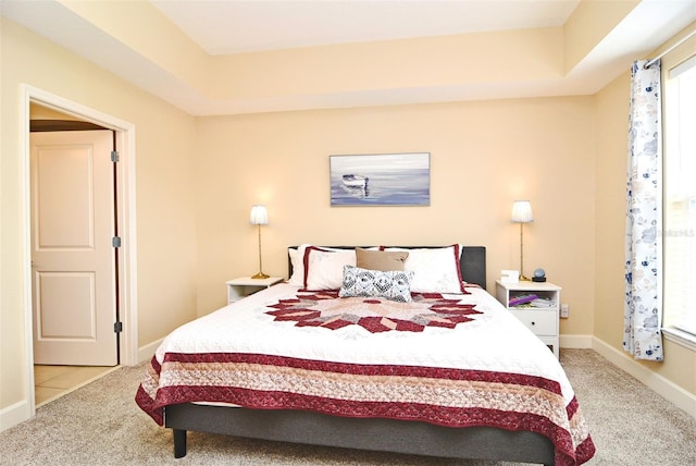 bedroom with light colored carpet and a tray ceiling