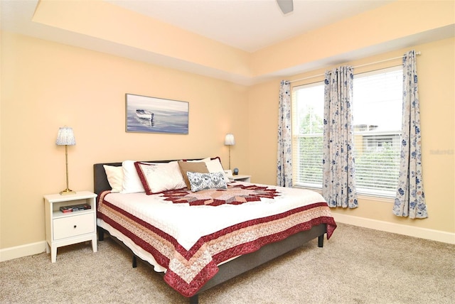 carpeted bedroom with a raised ceiling and ceiling fan