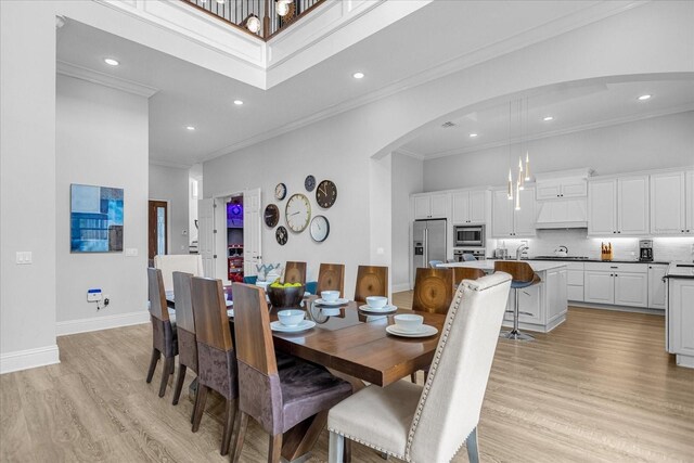 dining room with a towering ceiling, sink, ornamental molding, and light hardwood / wood-style flooring