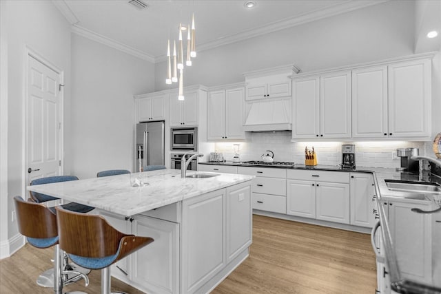 kitchen featuring premium range hood, sink, pendant lighting, stainless steel appliances, and a kitchen island with sink