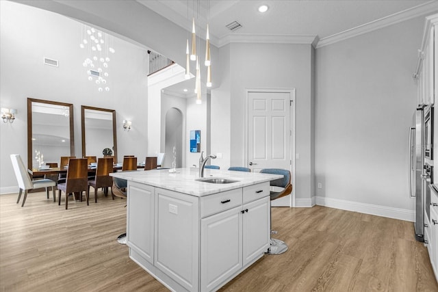 kitchen featuring sink, light stone counters, a center island with sink, pendant lighting, and white cabinets