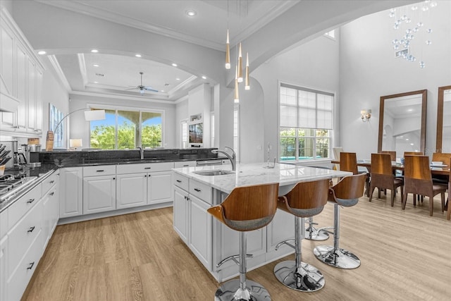 kitchen featuring an island with sink, sink, dark stone countertops, white cabinets, and light hardwood / wood-style flooring