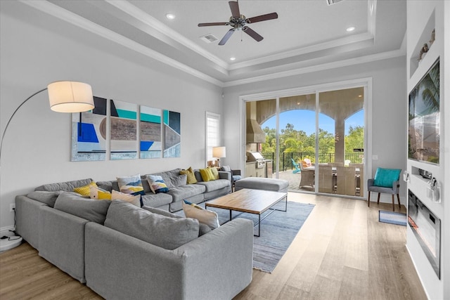 living room featuring light hardwood / wood-style flooring, ornamental molding, a raised ceiling, and ceiling fan