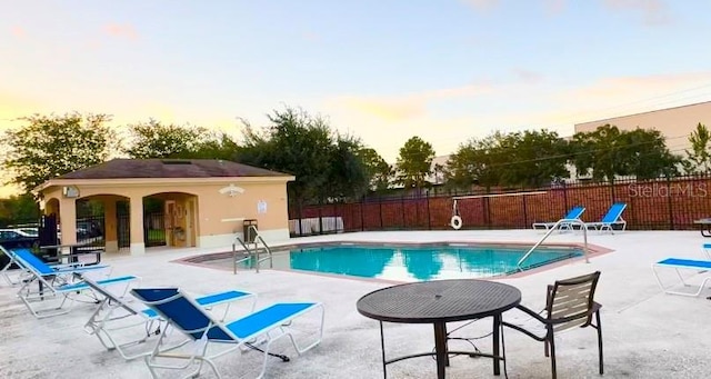 pool at dusk featuring a patio area and an outdoor structure