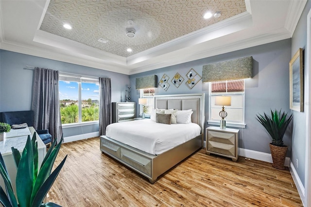 bedroom with light wood-type flooring, a tray ceiling, and ornamental molding