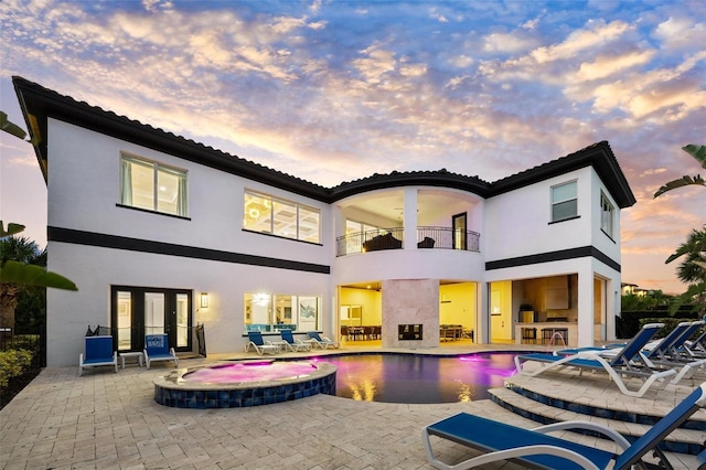 back house at dusk featuring a swimming pool with hot tub, a balcony, a bar, and a patio