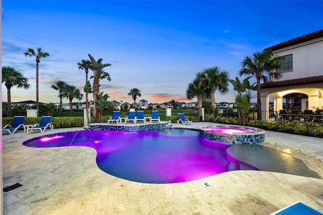 pool at dusk featuring a patio area, an in ground hot tub, and pool water feature