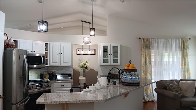 kitchen with tasteful backsplash, stainless steel appliances, hanging light fixtures, white cabinets, and lofted ceiling