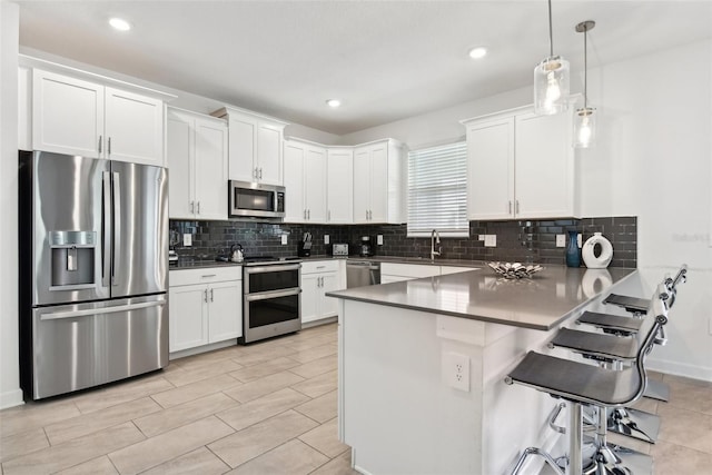 kitchen with a breakfast bar, appliances with stainless steel finishes, white cabinetry, and hanging light fixtures