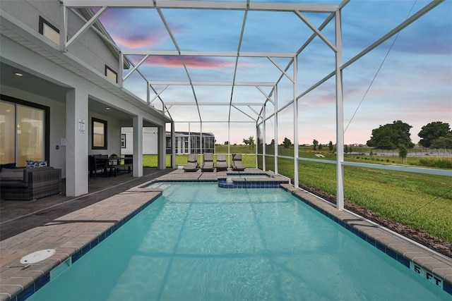 pool at dusk with a lawn, a patio area, an in ground hot tub, and glass enclosure