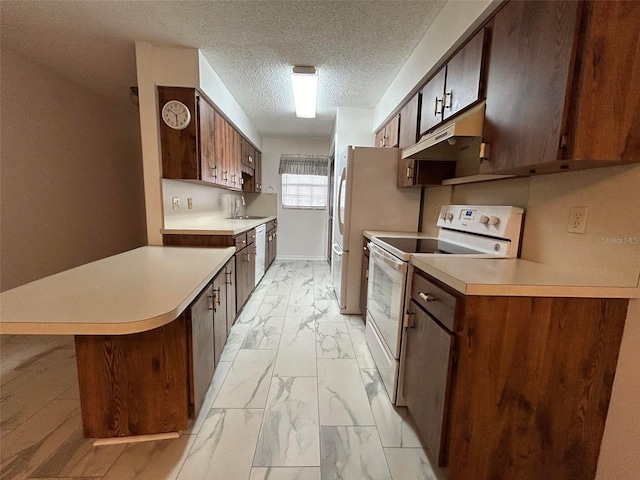 kitchen featuring sink, white appliances, a textured ceiling, a kitchen bar, and kitchen peninsula