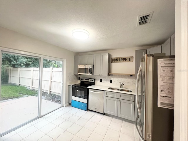 kitchen with gray cabinetry, sink, light tile patterned floors, and appliances with stainless steel finishes