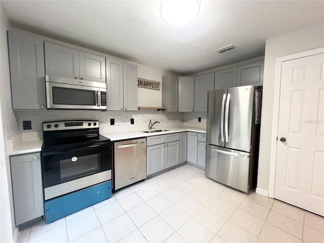 kitchen featuring appliances with stainless steel finishes, a textured ceiling, sink, light tile patterned floors, and gray cabinets