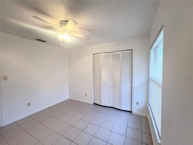 unfurnished bedroom with ceiling fan, light tile patterned flooring, a textured ceiling, and a closet