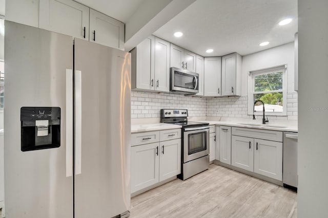 kitchen featuring sink, tasteful backsplash, light wood-type flooring, appliances with stainless steel finishes, and white cabinets