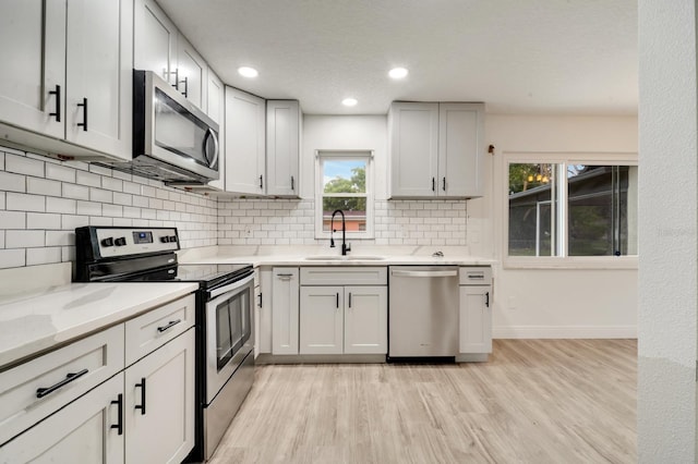 kitchen with sink, decorative backsplash, light stone counters, stainless steel appliances, and light hardwood / wood-style flooring