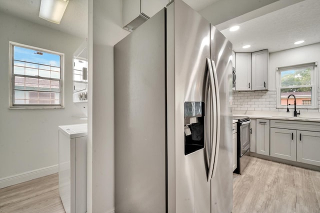 kitchen with sink, light hardwood / wood-style flooring, appliances with stainless steel finishes, backsplash, and plenty of natural light