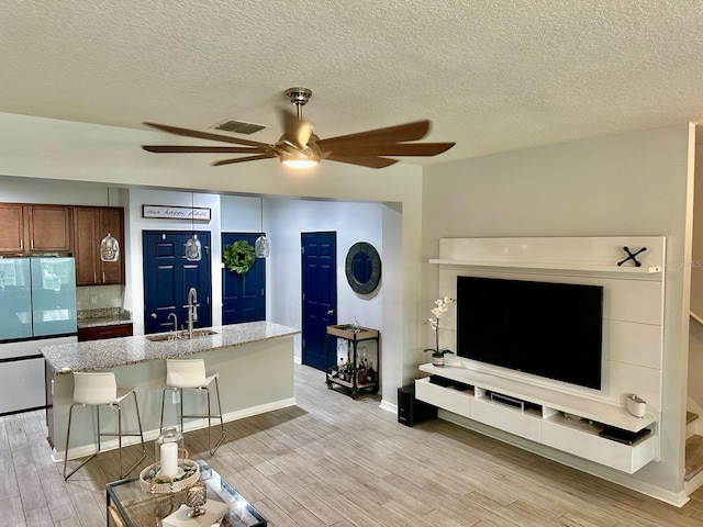 living room with ceiling fan, light hardwood / wood-style floors, a textured ceiling, and sink