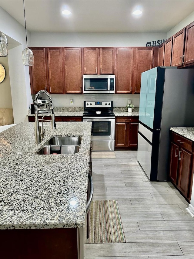 kitchen featuring hanging light fixtures, light wood-type flooring, appliances with stainless steel finishes, light stone countertops, and sink