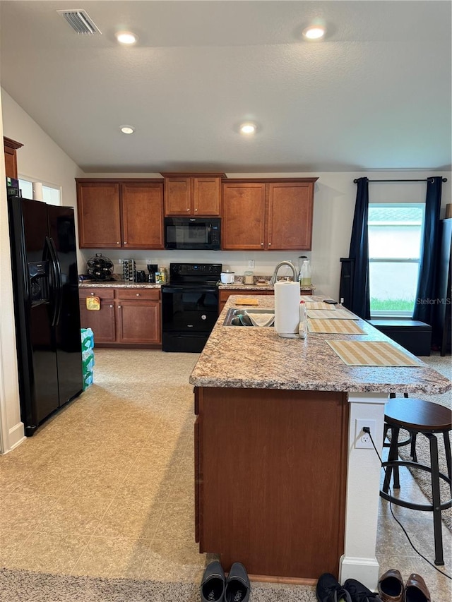 kitchen with sink, a breakfast bar area, a kitchen island with sink, light stone counters, and black appliances