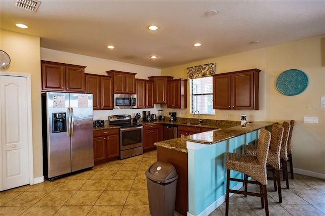 kitchen featuring appliances with stainless steel finishes, kitchen peninsula, dark stone counters, a breakfast bar, and sink