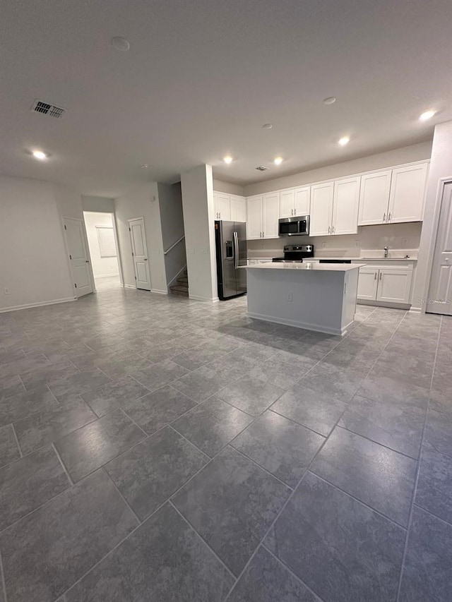 kitchen featuring stainless steel appliances, white cabinetry, a kitchen island, and sink