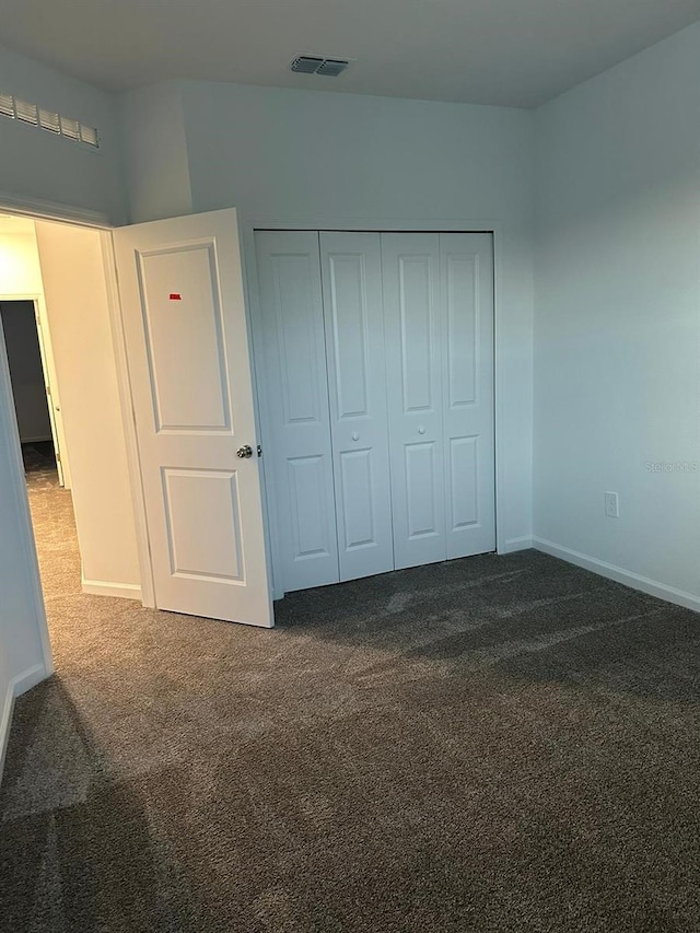 unfurnished bedroom featuring dark carpet and a closet