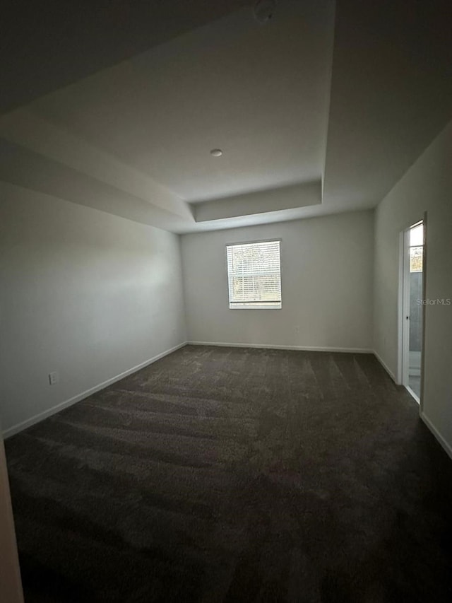 spare room with dark carpet and a raised ceiling