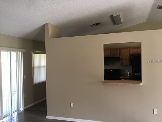 spare room with dark wood-type flooring, vaulted ceiling, and a textured ceiling