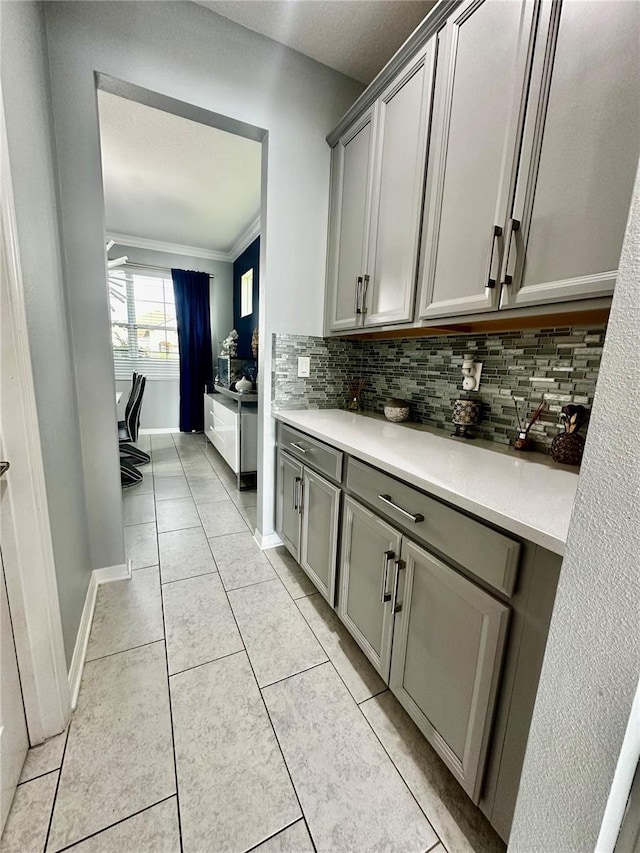 kitchen featuring gray cabinetry, light tile patterned floors, tasteful backsplash, and ornamental molding