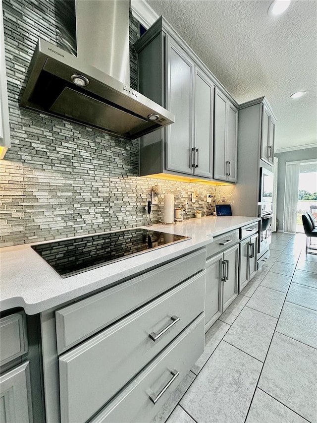 kitchen with light tile patterned flooring, gray cabinetry, tasteful backsplash, black electric stovetop, and wall chimney range hood