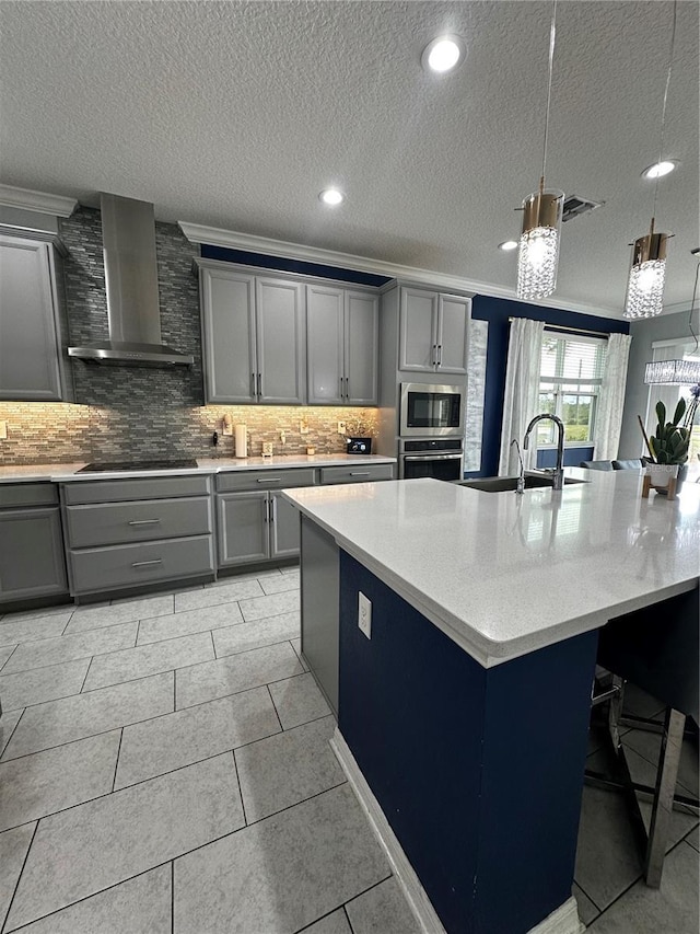 kitchen featuring sink, gray cabinets, a kitchen island with sink, stainless steel appliances, and wall chimney exhaust hood