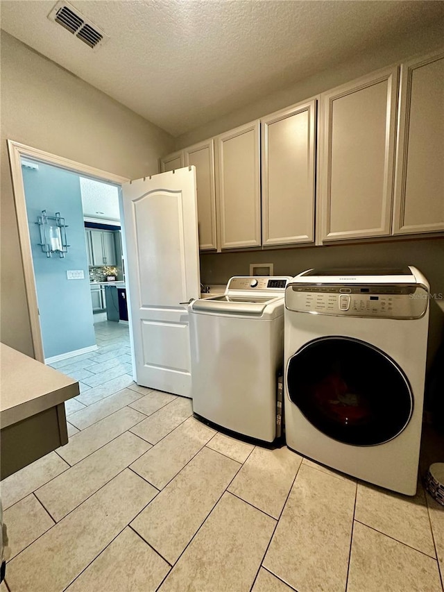 laundry area with cabinets, light tile patterned floors, washing machine and clothes dryer, and a textured ceiling