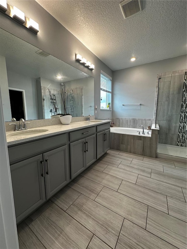 bathroom featuring independent shower and bath, vanity, and a textured ceiling