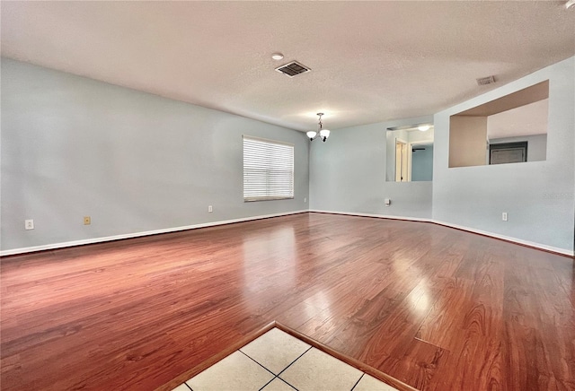 empty room with a textured ceiling, wood-type flooring, and a chandelier